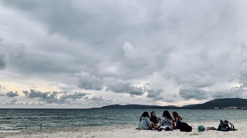 People sitting on beach by sea against sky
