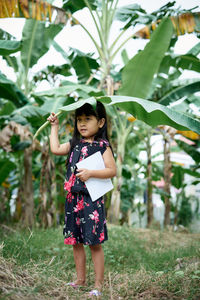 Full length of cute girl holding banana leaf outdoors