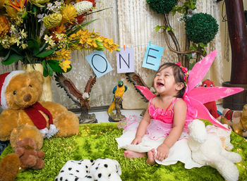 Cheerful shirtless baby girl sitting amidst stuffed toys during birthday
