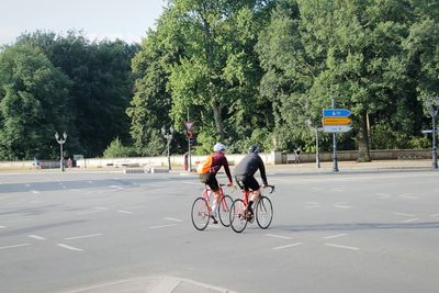 Rear view of cyclists riding on road against trees