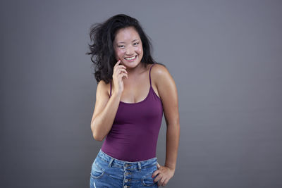 Portrait of young woman standing against gray background