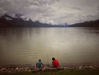 Rear view of men sitting on lake against sky
