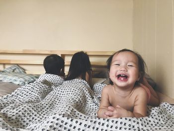 Portrait of cheerful baby girl lying with siblings on bed