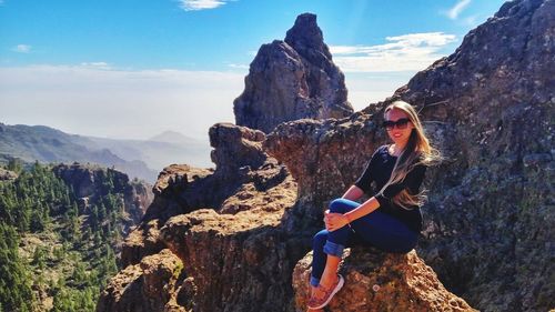 Portrait of smiling beautiful woman sitting on rock against mountain