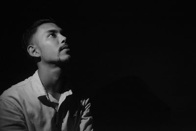 Portrait of young man looking away against black background