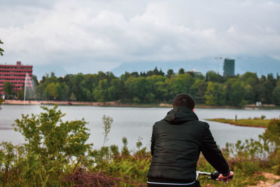 Rear view of man looking at lake against sky