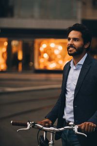 Smiling man with bicycle looking away while standing in city