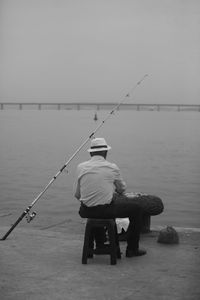 Rear view of man fishing in sea against sky