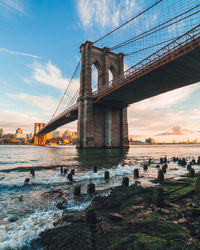 Low angle view of brooklyn bridge over river against sky