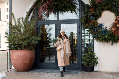 A stylish young woman in a hat and coat with branches of nobilis leaves the cafe