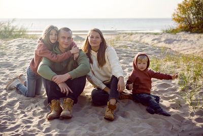 Family with a son and daughter and a dog sit on the sand in autumn