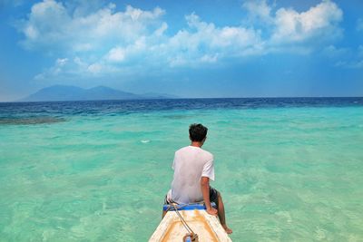 Rear view of young man sitting in boat on sea against blue sky