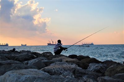 Man fishing in sea against sky during sunset