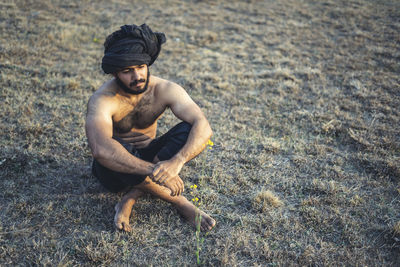 Young indian farmer standing on a barren field. crops not growing due to shortage of rain.