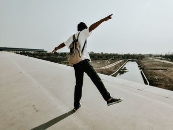 Rear view of woman with arms outstretched standing against sky