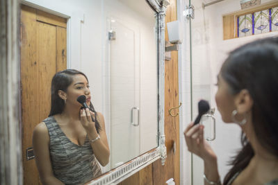 Young woman applying makeup in her bathroom mirror