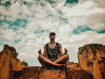 Portrait of young man sitting on rock against sky