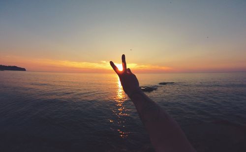 Silhouette man showing peace sign by sea during sunset