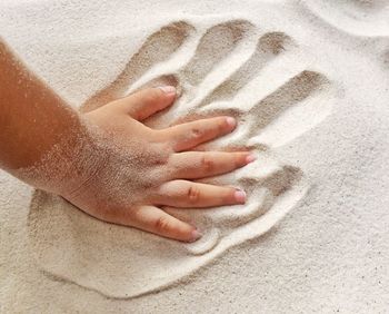 Cropped hand of child on sand at beach
