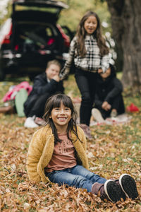 Portrait of smiling girl sitting on autumn leaves during picnic