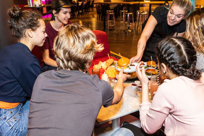 Smiling waitress serving food to multi-ethnic teenagers sitting at restaurant