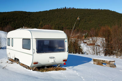 Camper van on snow covered field by mountains in sunny day