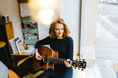 High angle view of young woman playing guitar by window at home