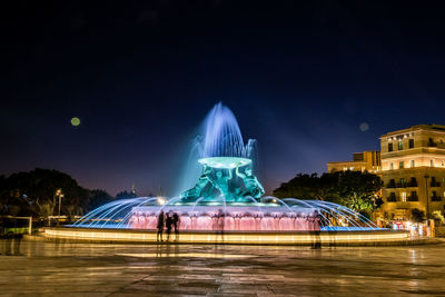 Illuminated fountain against sky at night