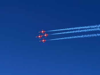 Low angle view of airplane flying patrouille suisse against clear blue sky