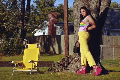 Full length of fashionable teenage girl standing by tree trunk