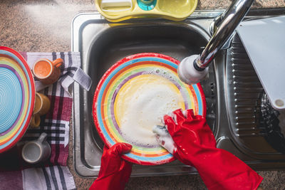 Mature woman wearing gloves washing dishes at home