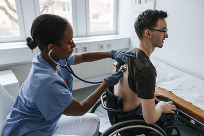 Teenage boy's back getting checked with stethoscope by female doctor in examination room at clinic