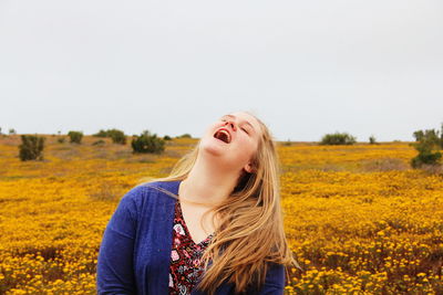 Young woman with flowers in field against clear sky