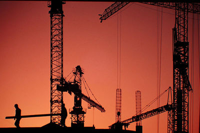 Silhouette of cranes against sky at sunset