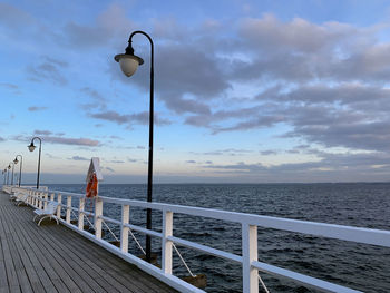 Street lights on pier by sea against sky