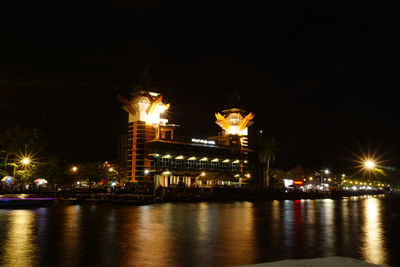 Illuminated city by river against sky at night