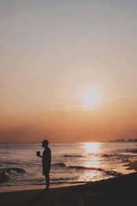 Silhouette man standing on beach against sky during sunset