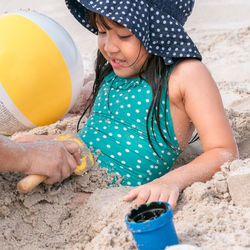 Cropped hands covering playful girl with sand at beach