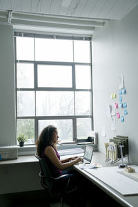 Side view of businesswoman using laptop computer at desk in office