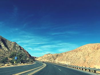 Empty road by mountains against blue sky