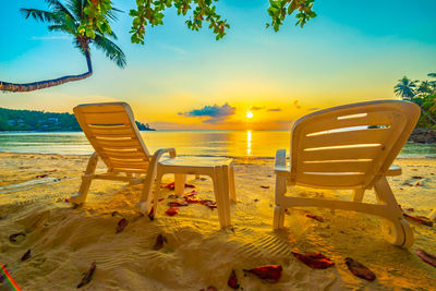 Beautiful tropical sunset  two sun beds, loungers under palm tree sand sea view beach resort hotel