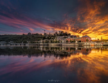 Scenic view of lake by buildings against sky during sunset