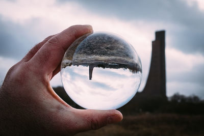 Cropped hand holding crystal ball with reflection against cloudy sky