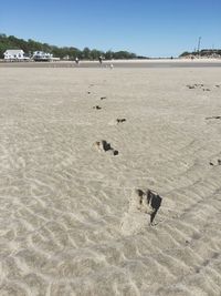 Footprints on sand at beach against clear sky