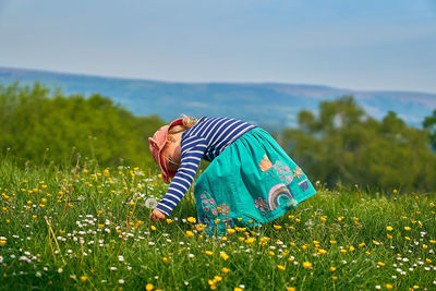 Side view of girl picking flowers while standing on land