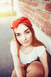 Portrait of young woman wearing red bandana by brick wall