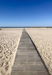 Boardwalk leading towards beach against clear blue sky