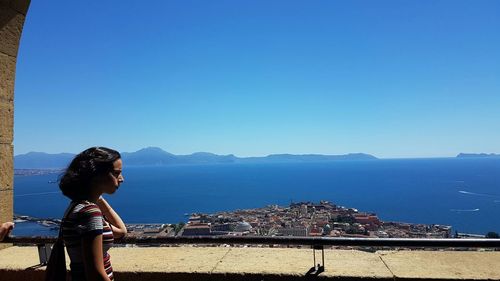 Woman standing by sea against clear blue sky