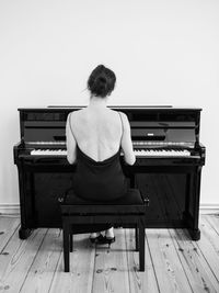 Rear view of young woman playing piano at home