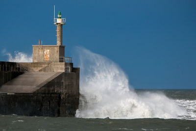 Wave splashing on lighthouse in sea against clear sky